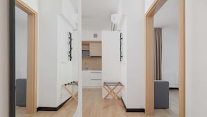 Ein modernes, minimalistisches Zimmer mit Holzboden, einer grauen Couch und einer kleinen Küchenzeile im Hintergrund.