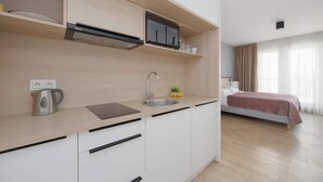 Une cuisine moderne équipée d’un four à micro-ondes, d’une bouilloire et d’un évier intégrés. La pièce adjacente contient un lit recouvert d’une couverture rouge.