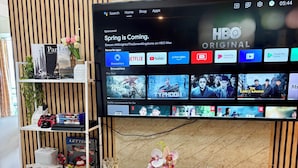 Een restaurantruimte in een hotel, met een televisie waarop HBO wordt getoond, een net gedekte eettafel met borden en bestek, en een plank met diverse voorwerpen, waaronder een boek en een bloemenvaas.