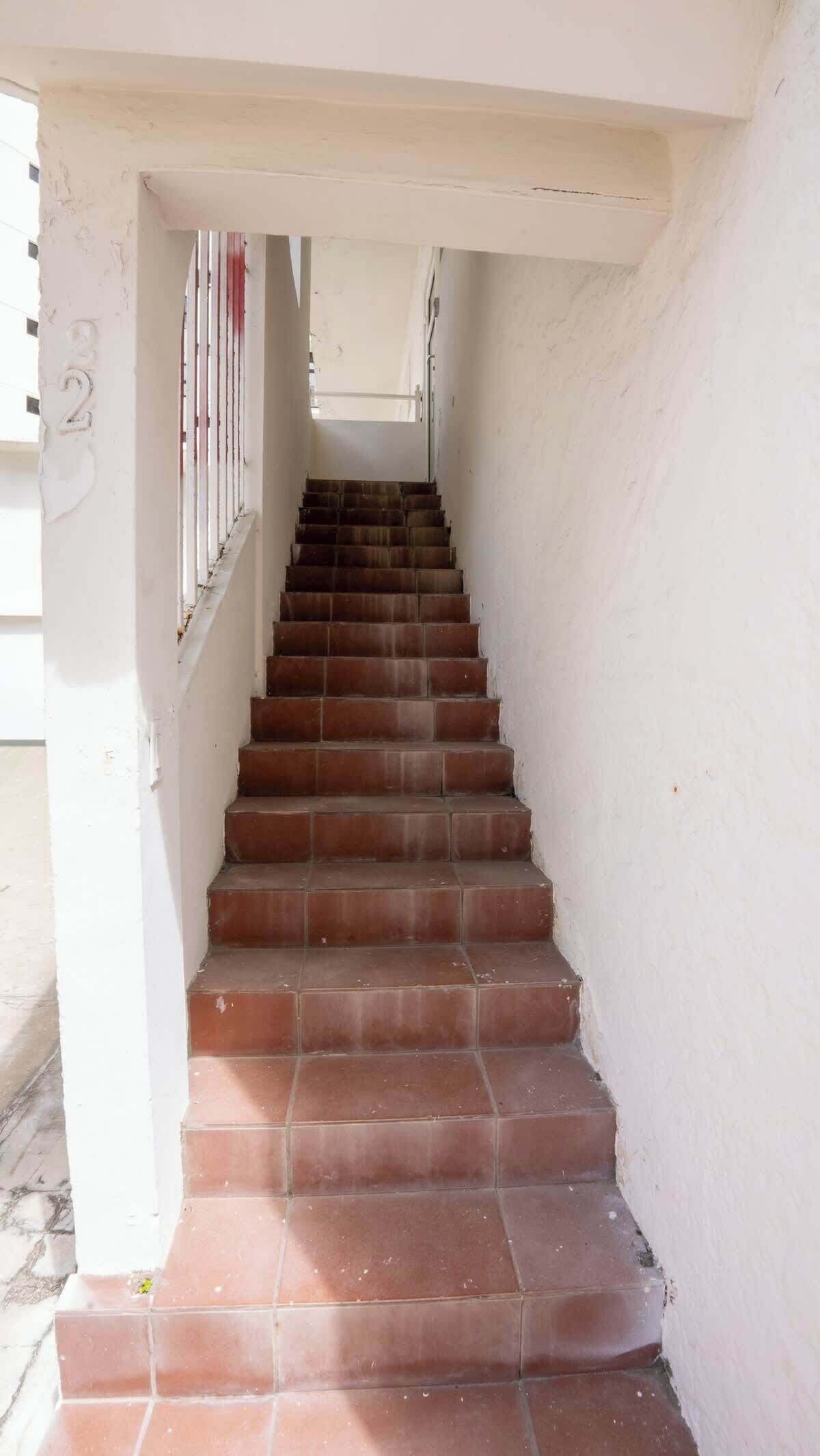 Un escalier menant à l’étage supérieur, avec des murs blancs et le chiffre « 2 » bien visible sur le côté gauche.