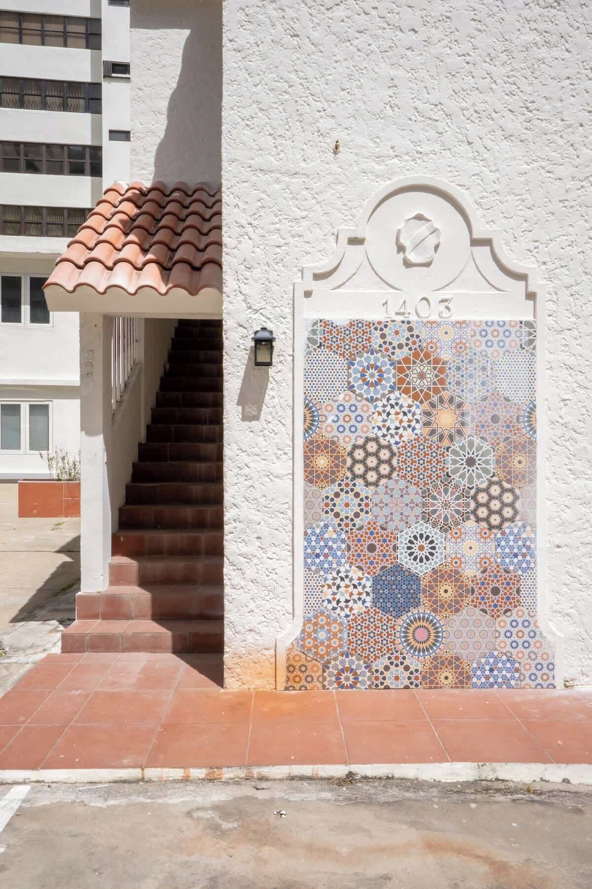 Una entrada de edificio con un portón de azulejos, una escalera y una pared blanca.