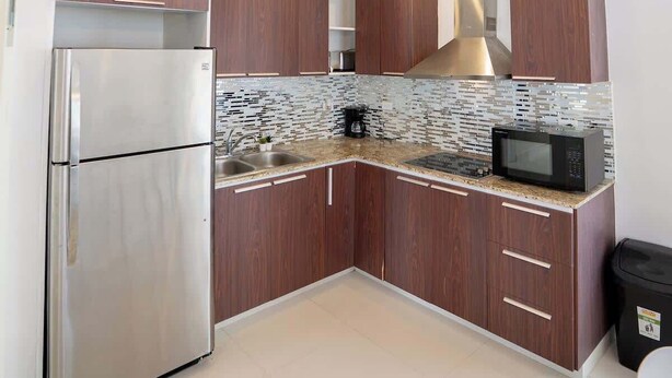 A modern kitchen with wooden cabinets, stainless steel appliances, and a tiled backsplash. - 3Bedroom Apt. Walking To The Beach C.2 (San Juan)