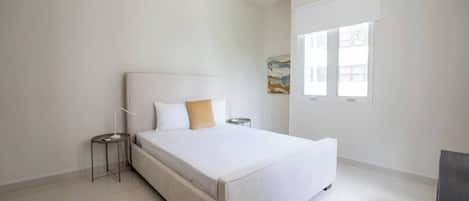 Een minimalistische slaapkamer met een bed, nachtkastje en raam.