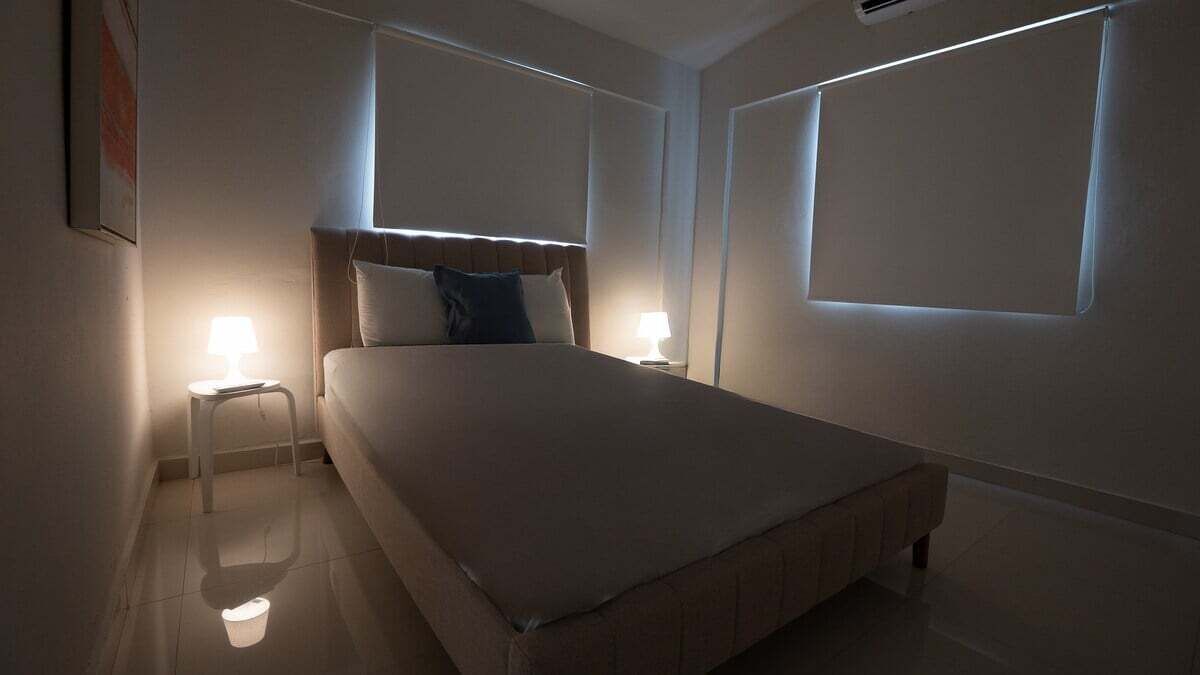 Quarto de hotel com cama, abajures, uma janela e ar condicionado fixado na parede.