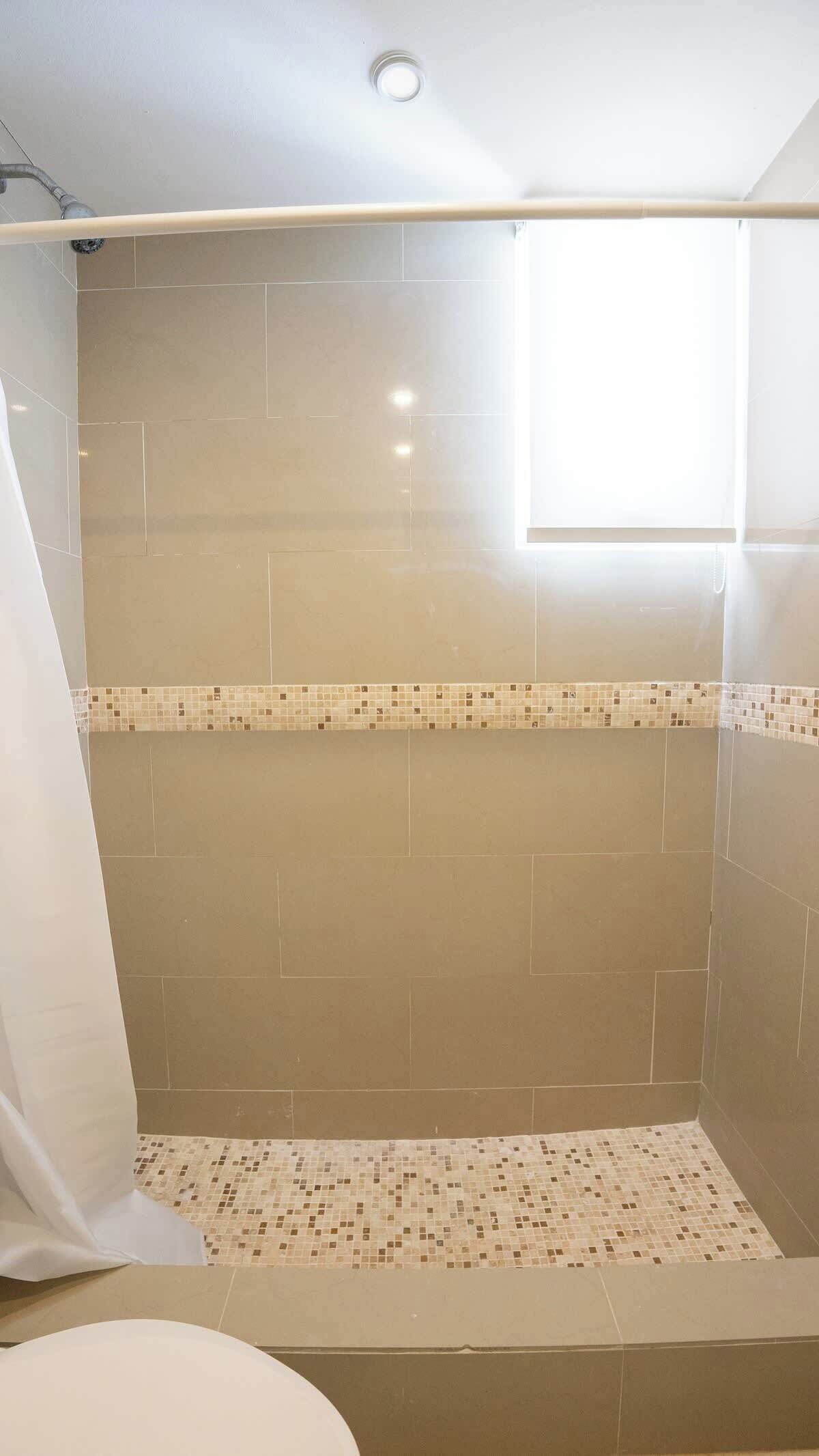 A bathroom with a shower area, tiled walls, and a window.