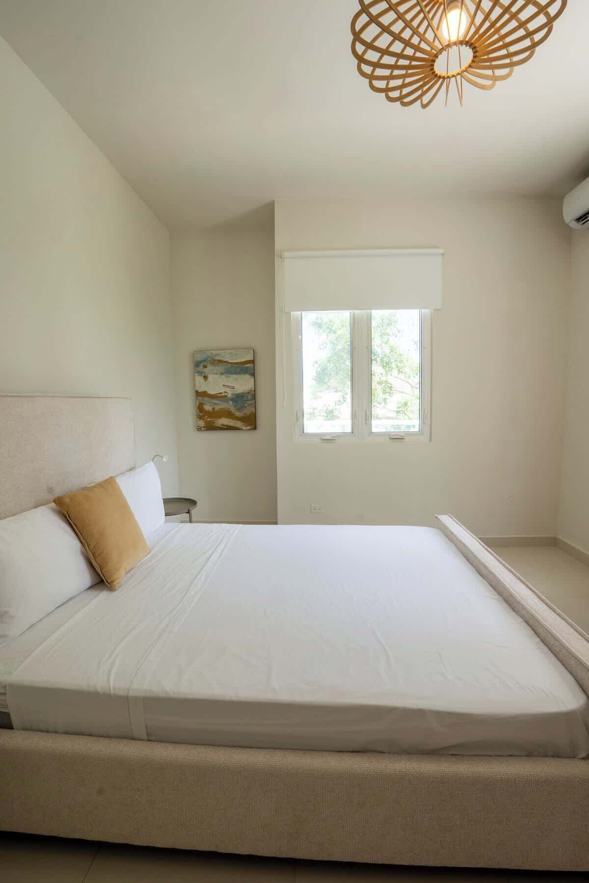 Un dormitorio con cama, ventana y lámpara de pared.