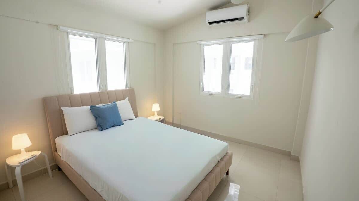 Een hotelkamer met een bed, twee bedlampen, een raam en een airconditioning.