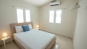 A hotel room with a bed, two bedside lamps, a window, and an air conditioning unit. - 3Bedroom Apt. Walking To The Beach C.2 (San Juan)