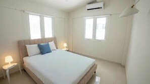Ein Hotelzimmer mit einem Bett, zwei Nachttischlampen, einem Fenster und einer Klimaanlage.