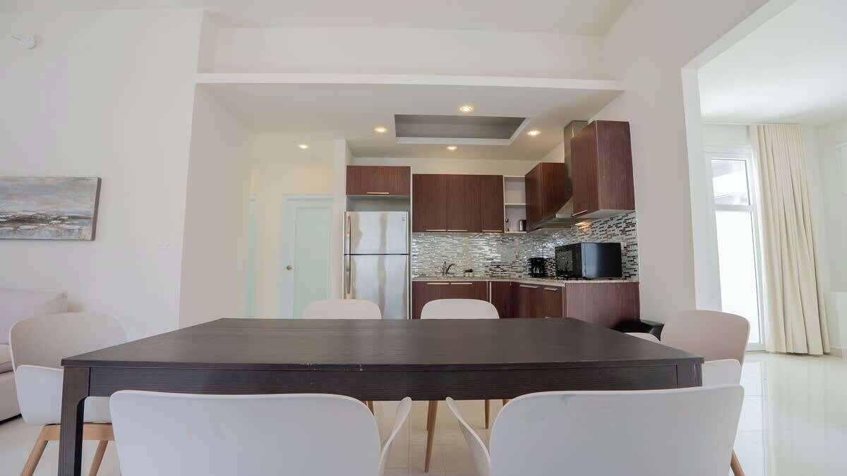 A modern kitchen with a dark countertop, white chairs, and a view into the dining area.