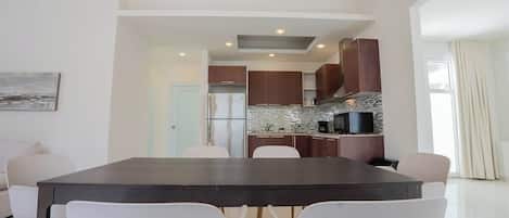 Una cocina moderna con encimera oscura, sillas blancas y vista al área de comedor.