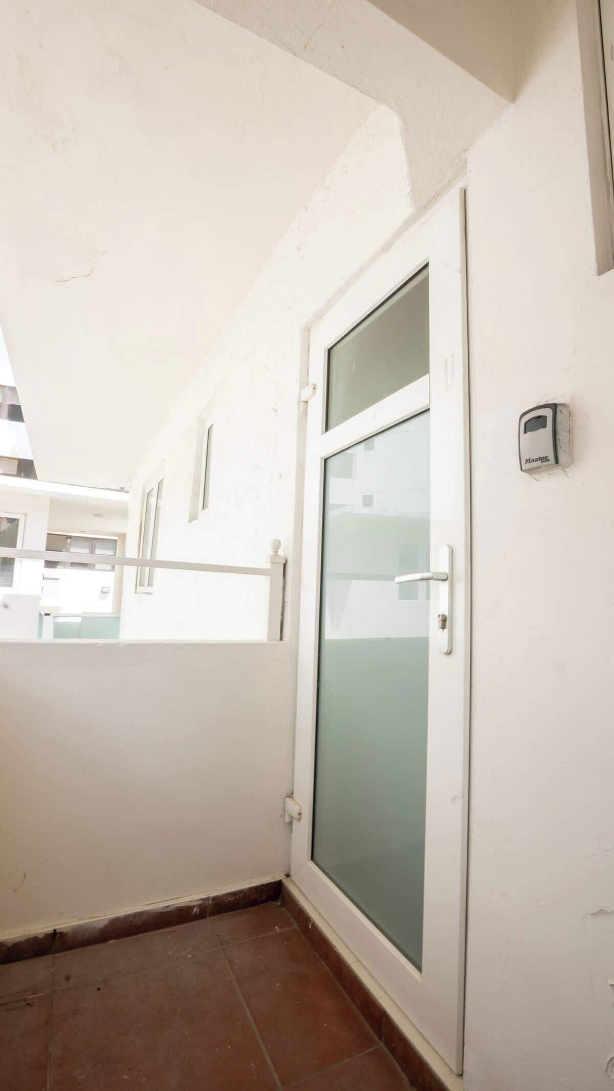 Una habitación con puerta de vidrio corredera, pared blanca y ventana visible.
