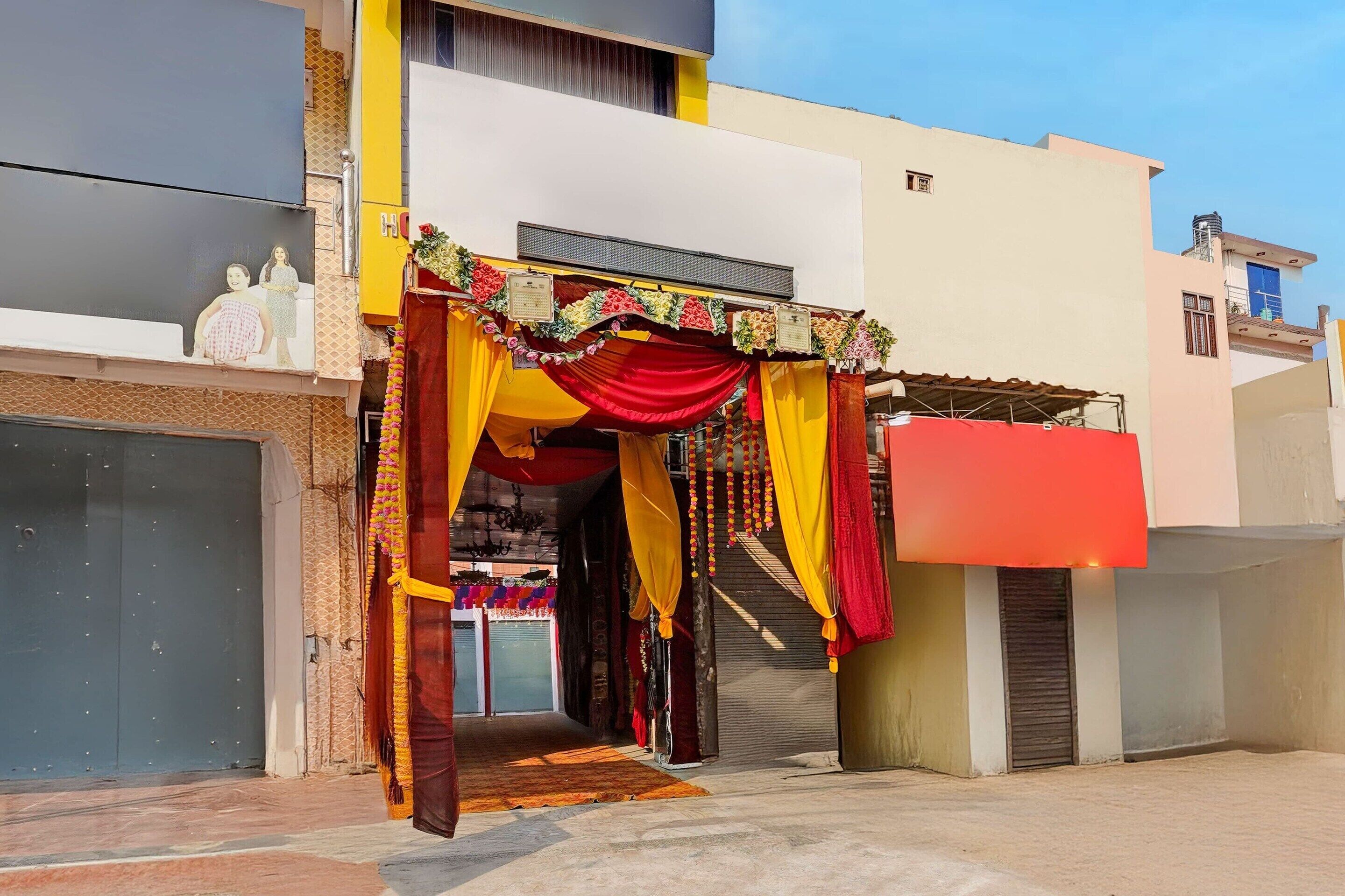 A building entrance with a red and yellow draped entrance, a closed garage door, and a clear sky.