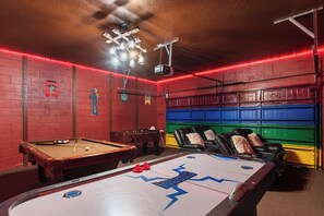 Ein Billardtisch mit 'Working'-Logo, ein Billardtisch und ein Kicker in einem Raum mit roten Backsteinwänden und farbenfrohen Stauraumelementen.