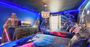 Ein Schlafzimmer mit Star Wars-Dekor, darunter eine Darth-Vader-Statue, ein Bett mit Galaxienmuster und ein Wandgemälde von Weltraumschlachten.