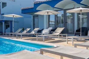 A poolside area with lounge chairs and umbrellas, a clear blue pool, and a building with blue and white exterior walls. - Hotel Santa Eulália Bay (Albufeira)