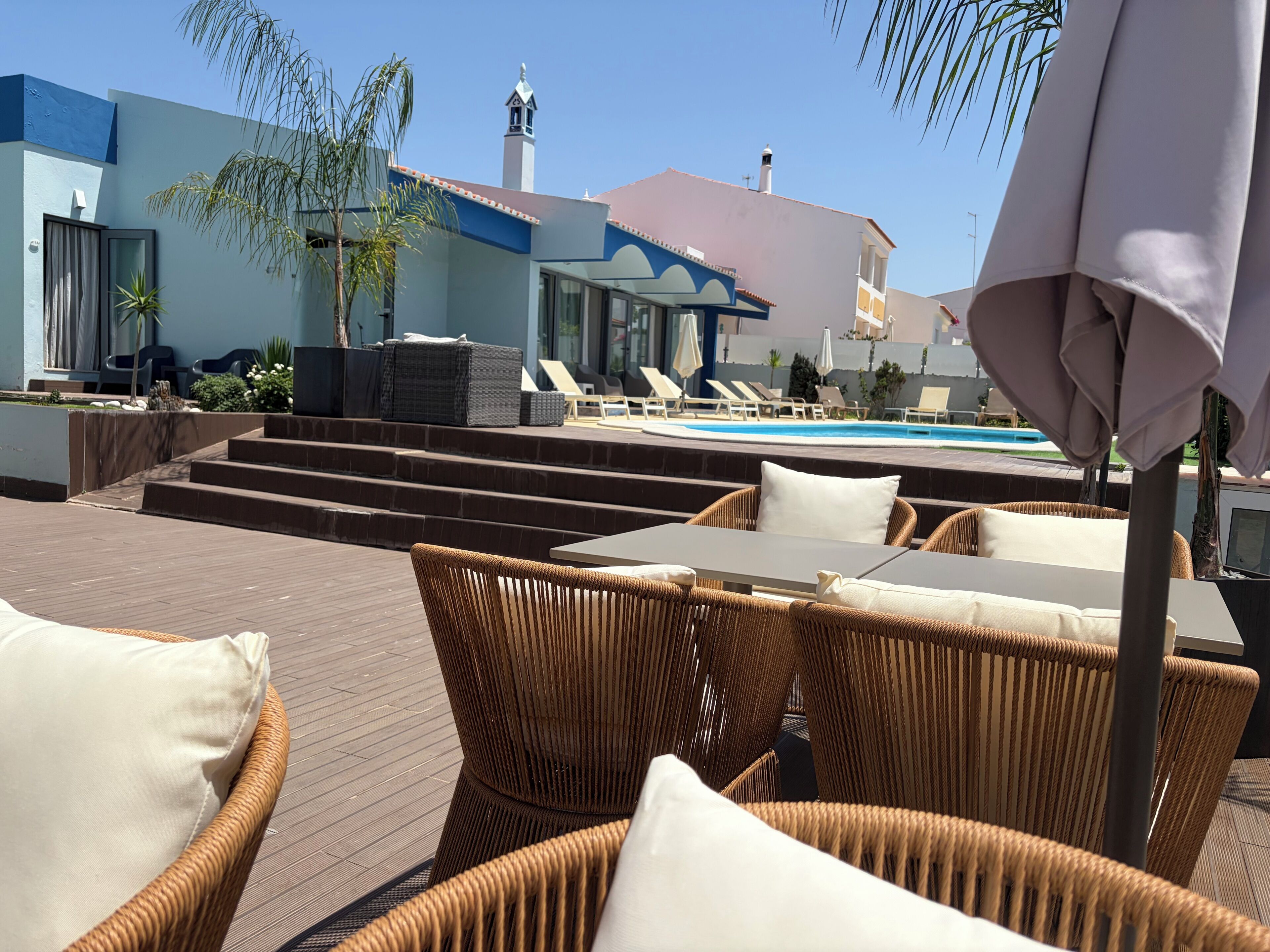 A poolside area with wicker furniture, a pool, and a building with a blue facade and a bell tower.