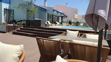 A poolside area with wicker furniture, a pool, and a building with a blue facade and a bell tower.