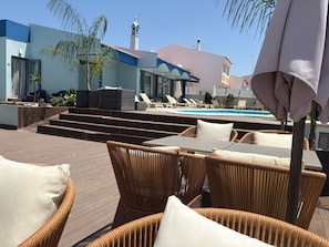 A poolside area with wicker furniture, a pool, and a building with a blue facade and a bell tower. - Hotel Santa Eulália Bay (Albufeira)