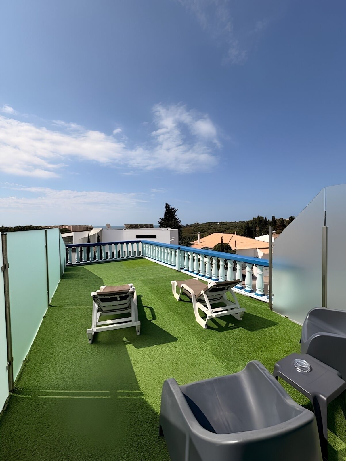 Terraza en la azotea con césped artificial, sillones blancos y barandilla azul.