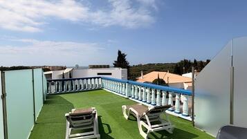 Terraza en la azotea con césped artificial, sillones blancos y barandilla azul.