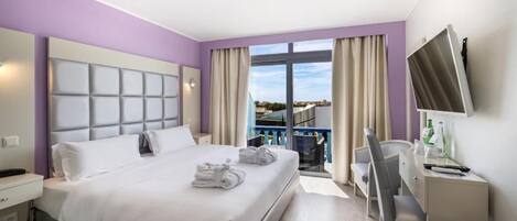 Habitación de hotel con cama, escritorio, silla, televisión y balcón con vistas.