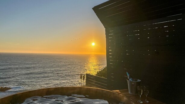 A sunset view from a balcony with a pool, a bottle, and glasses on the table. - Oceanfront Apartment Estudio el Suspiro (Tunquen)
