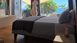 A bedroom with a large bed, a nightstand, a statue, and a view of the sea. - Oceanfront Apartment Estudio el Suspiro (Tunquen)