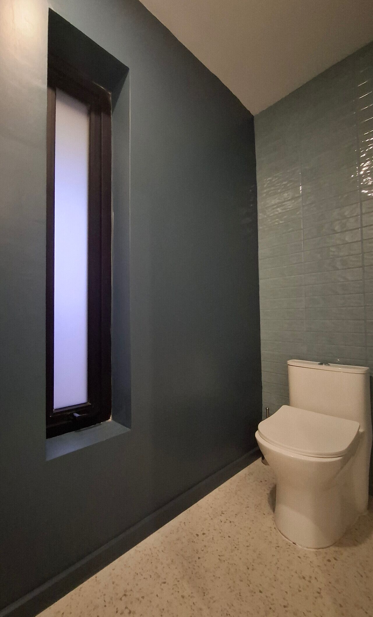 Un baño con inodoro, ventana y pared con azulejos.