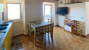 Un coin repas avec une table et des chaises en bois, un coin cuisine avec un évier et un plan de travail, et un téléviseur fixé au mur.
