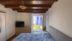 Une chambre à coucher avec un lit, un téléviseur posé sur une commode et un balcon donnant sur un paysage verdoyant.