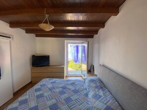 A bedroom with a bed, a television on a dresser, and a balcony with a view of greenery. - Apartment "Casa dai Nonni" Cozy apartment with beautiful lake view (Perledo)
