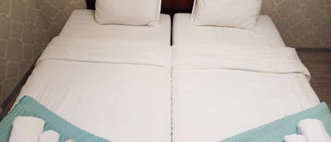 A double bed with white linens, two pillows, and a teal-patterned bed runner.