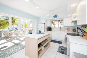 A bright kitchen with white cabinets, a microwave, and a sink. There is a wooden island with a plant and a blue fish decoration on the wall. - Barefoot Kai: Beach House w/Pool, Summer Kitchen, Dock + Kayaks, Steps to Rum Point Club! (Cayman Kai)