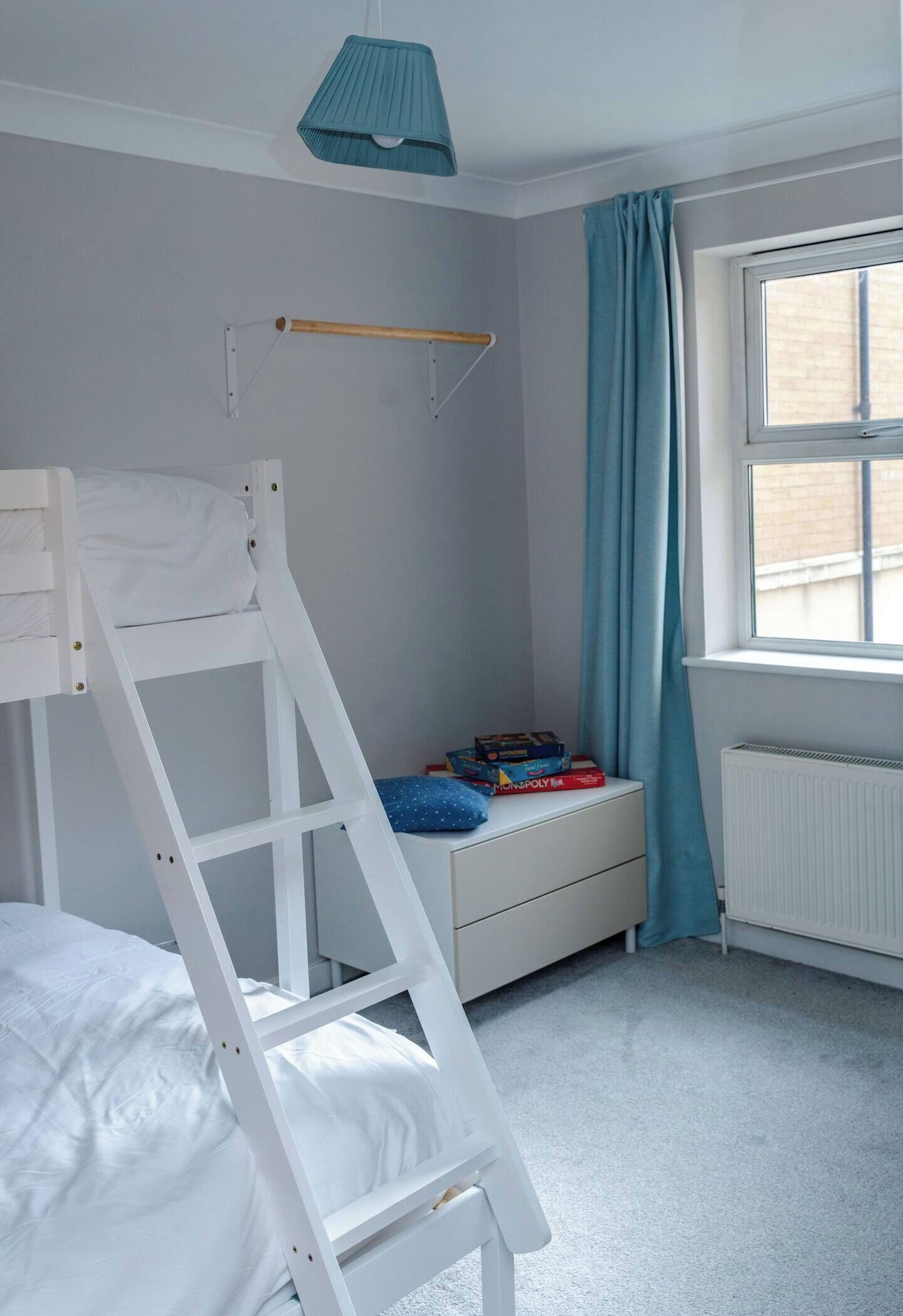 Een stapelbed met een hangplank, een raam met gordijnen en een radiator.