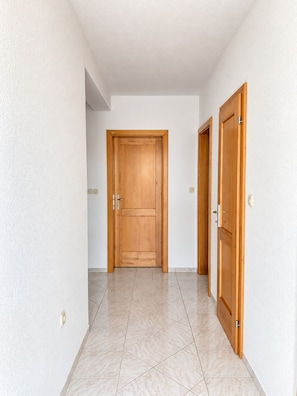 A hallway with a wooden door at the end, tiled floor, and white walls. - Apartment Vir 1 (Vir)