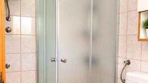 Ein Badezimmer mit Duschkabine aus Glas, einer weißen Toilette und einem wandmontierten Waschbecken.