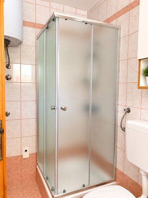A bathroom with a glass shower enclosure, a white toilet, and a wall-mounted sink. - Apartment Vir 1 (Vir)