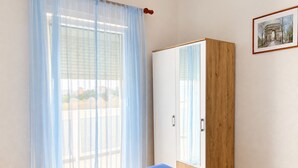 Une chambre à coucher avec un lit, une armoire et une fenêtre ornée de rideaux légers.
