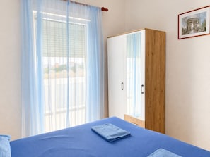 Ein Schlafzimmer mit einem Bett, einem Kleiderschrank und einem Fenster mit durchsichtigen Vorhängen.