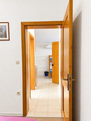 Ein Korridor mit Holztüren, die zu einem Raum mit Fliesenboden und einem blauen Mülleimer führen.