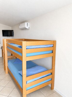 Ein Etagenbett mit blauer Bettwäsche, ein Flachbildfernseher und eine Klimaanlage an der Wand.
