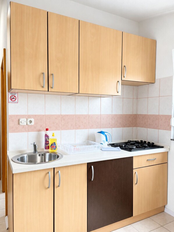 A kitchen with wooden cabinets, a stainless steel sink, a stove, and a kettle. - Apartment Vir 3 (Vir)