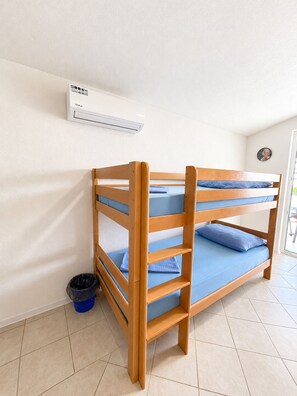 A bunk bed with a blue mattress and pillows, a white wall, a window, and a trash bin. - Apartment Vir 3 (Vir)
