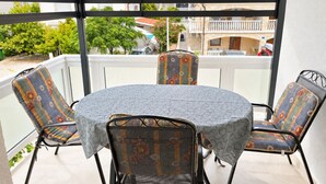 Un espace extérieur aménagé, abrité et doté d’une table ronde et de quatre chaises, offrant une vue sur un quartier résidentiel.