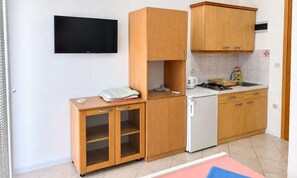 A compact kitchen with wooden cabinets, a built-in TV, and a small refrigerator. - Studio Apartment Vir 4 (Vir)
