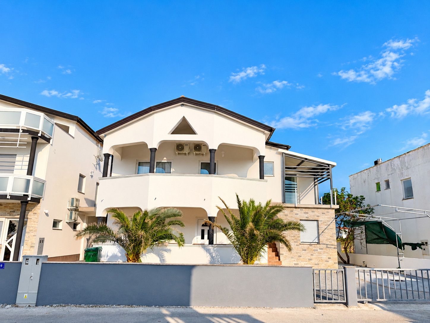 A two-story building with a balcony, a flat roof, and a gated entrance.
