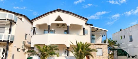A two-story building with a balcony, a flat roof, and a gated entrance.