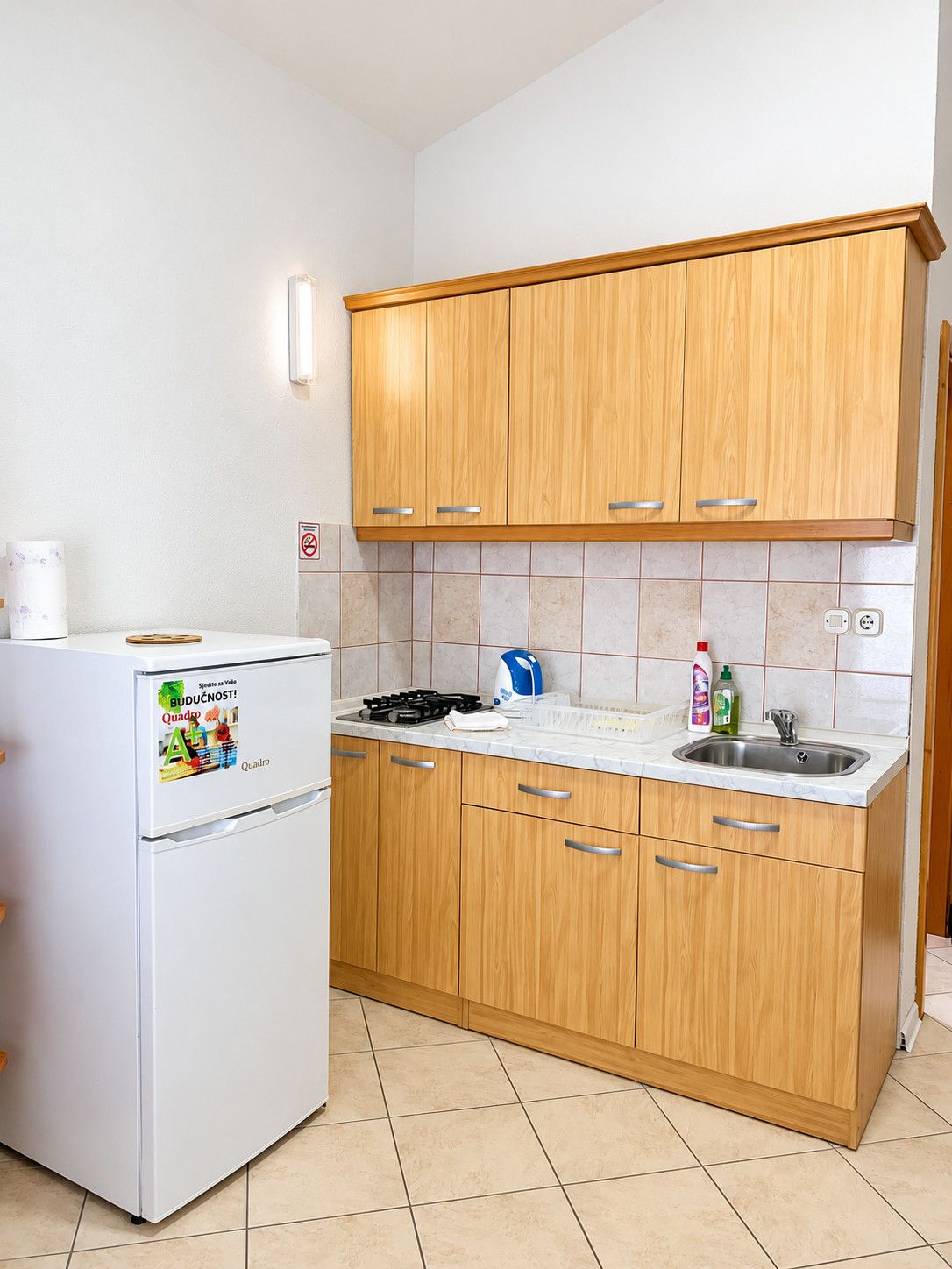 Eine kleine Küche mit Holzausstattung, einem weißen Kühlschrank, einem Gasherd und einem Spülbecken.
