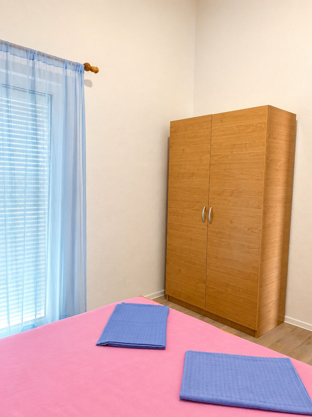 A room with a bed, a wardrobe, and a window with a curtain.